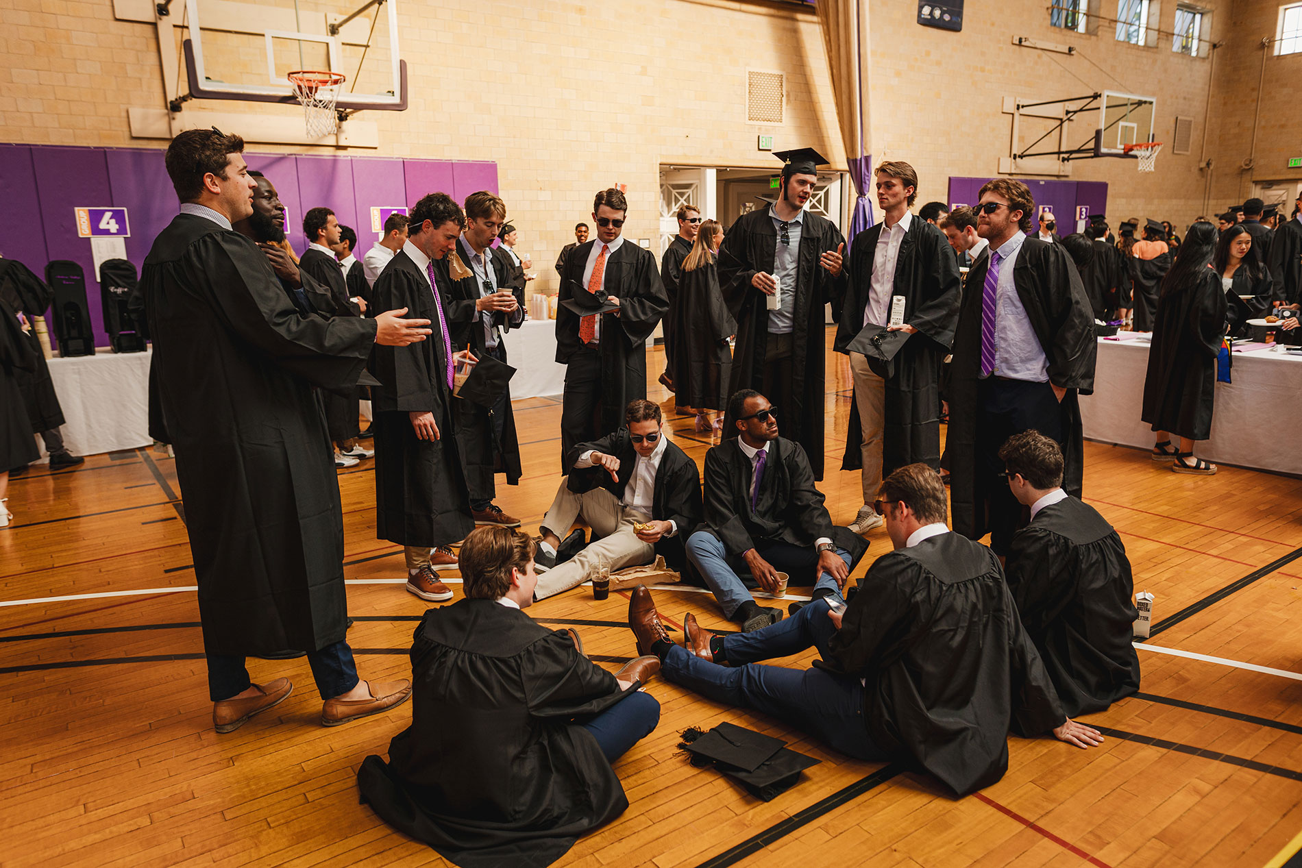 Graduates standing and sitting inside the Alumni Gym before Commencement.