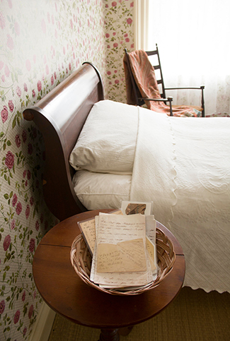 A bed with a table next to it filled with hand-written letters