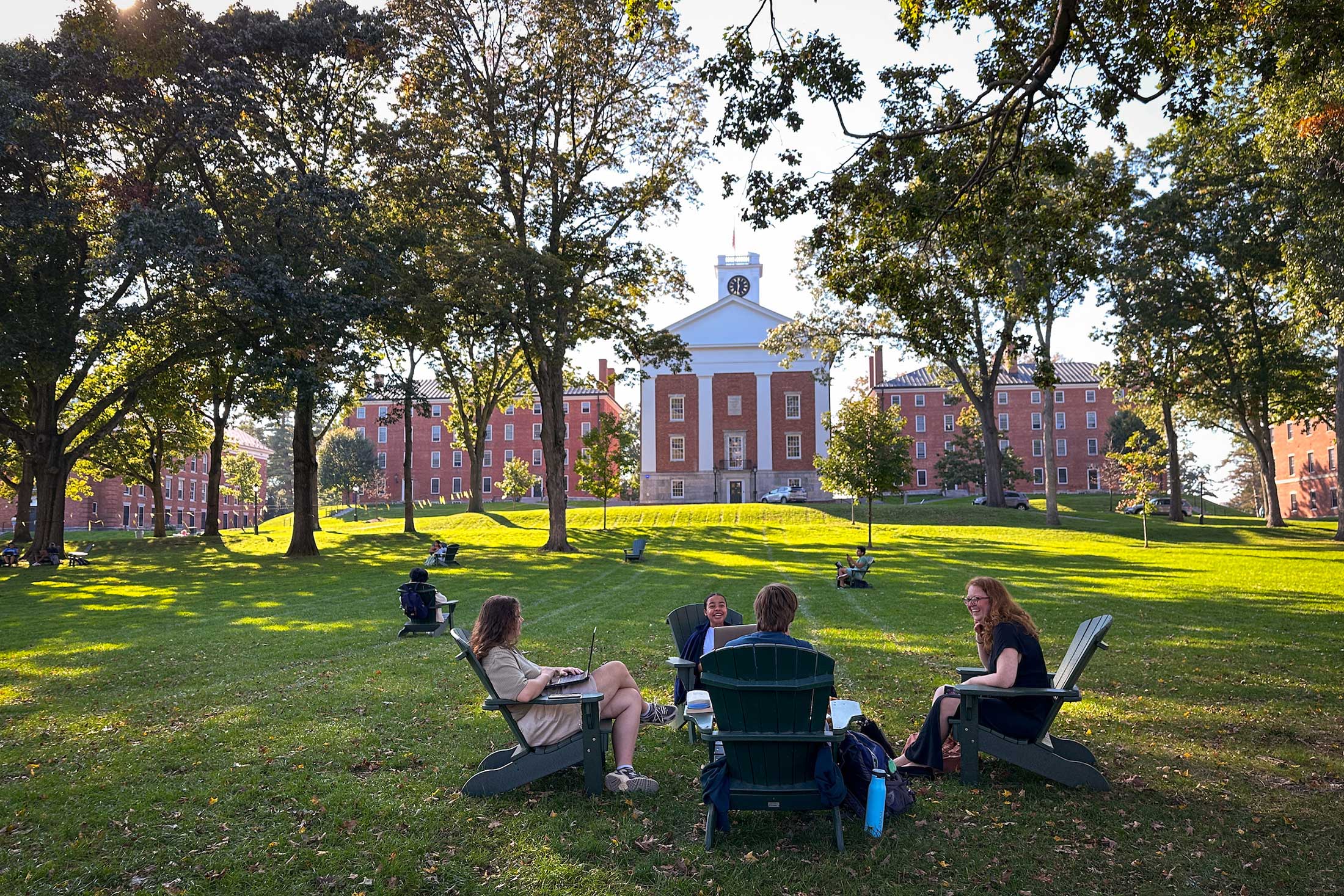 Four people sitting in Adirondack chairs on the Academic Quad in conversation.