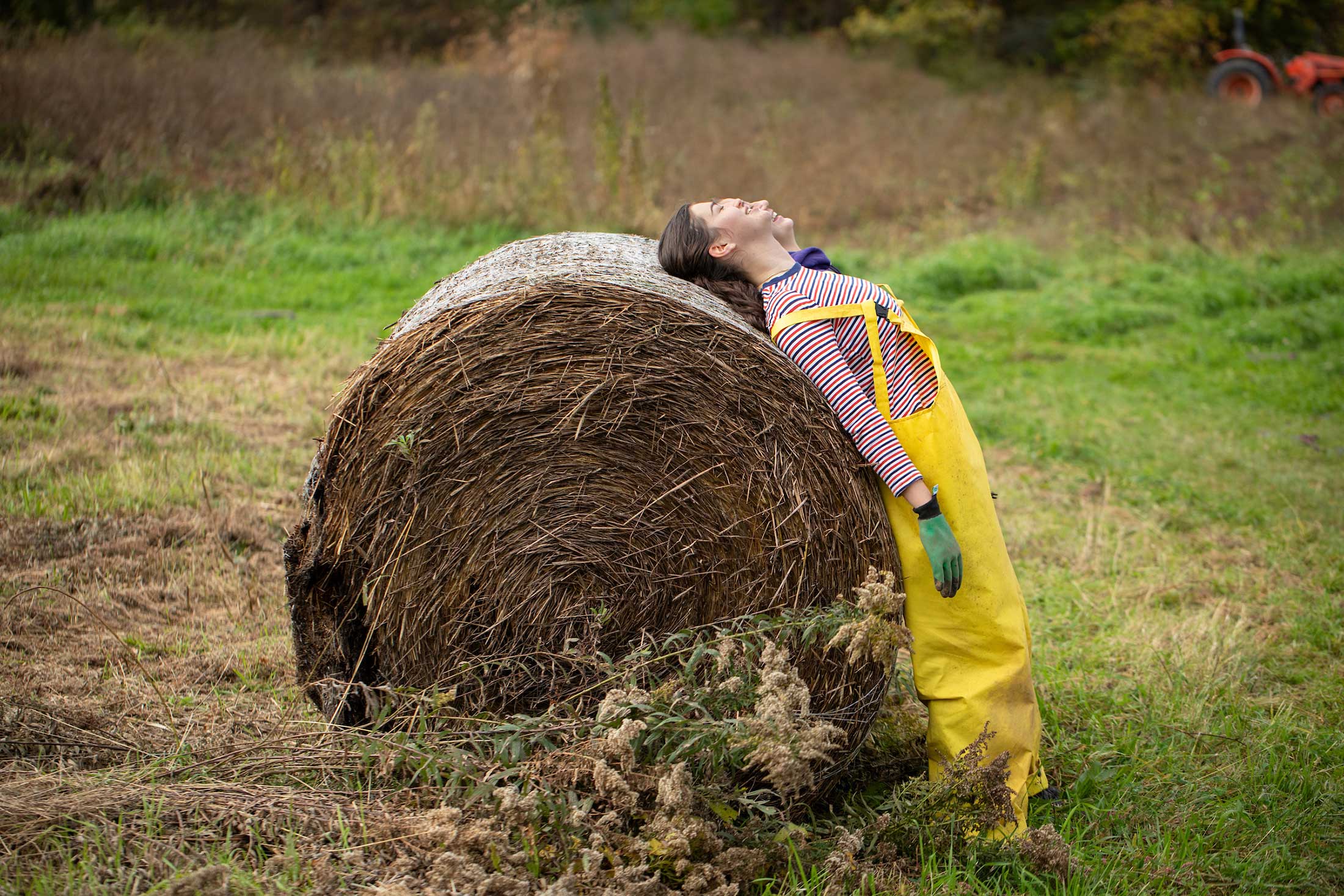 Two people lean backwards against a large cylinder of hay.