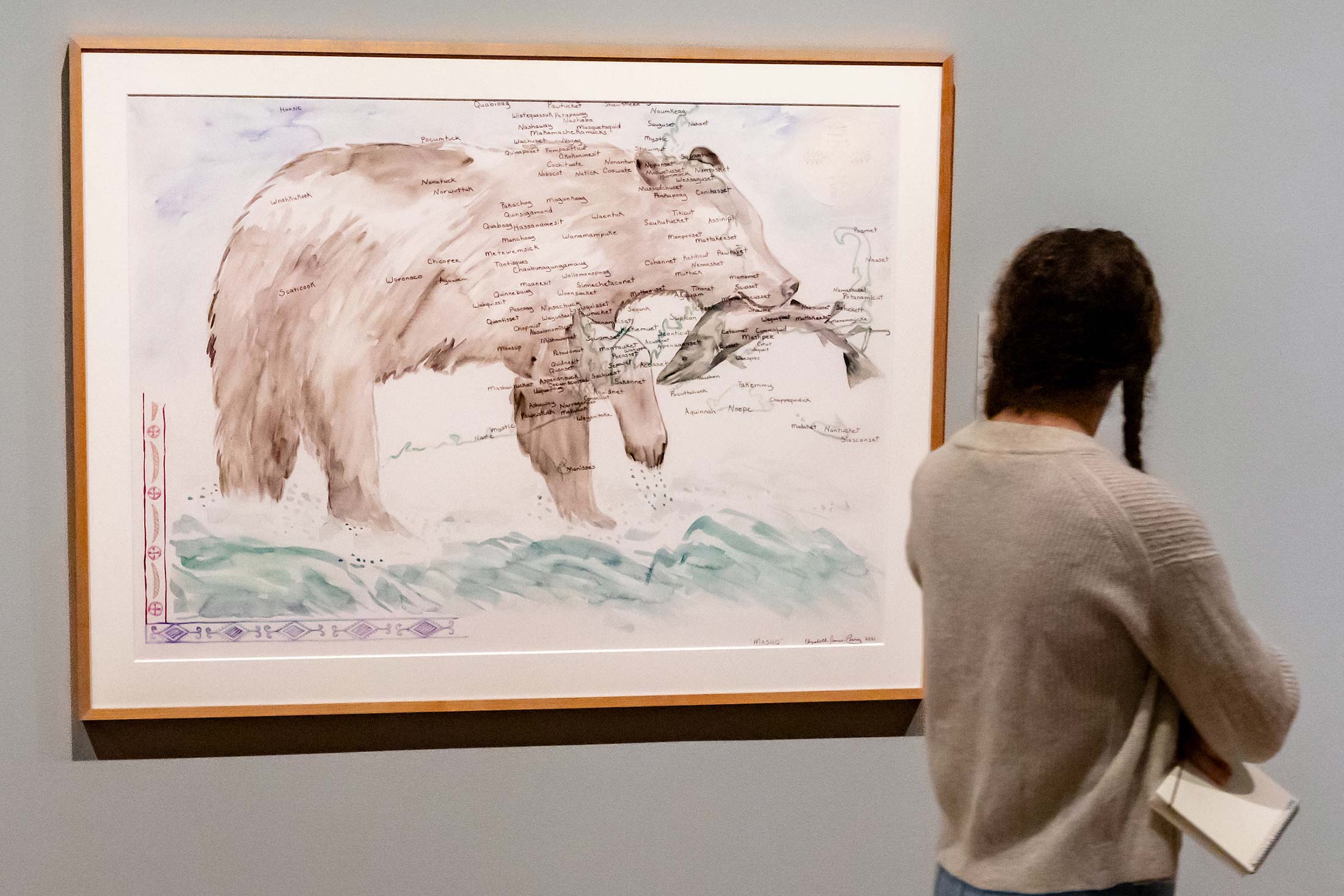 A woman looks at a painting of a map of Massachusetts shaped like a bear.
