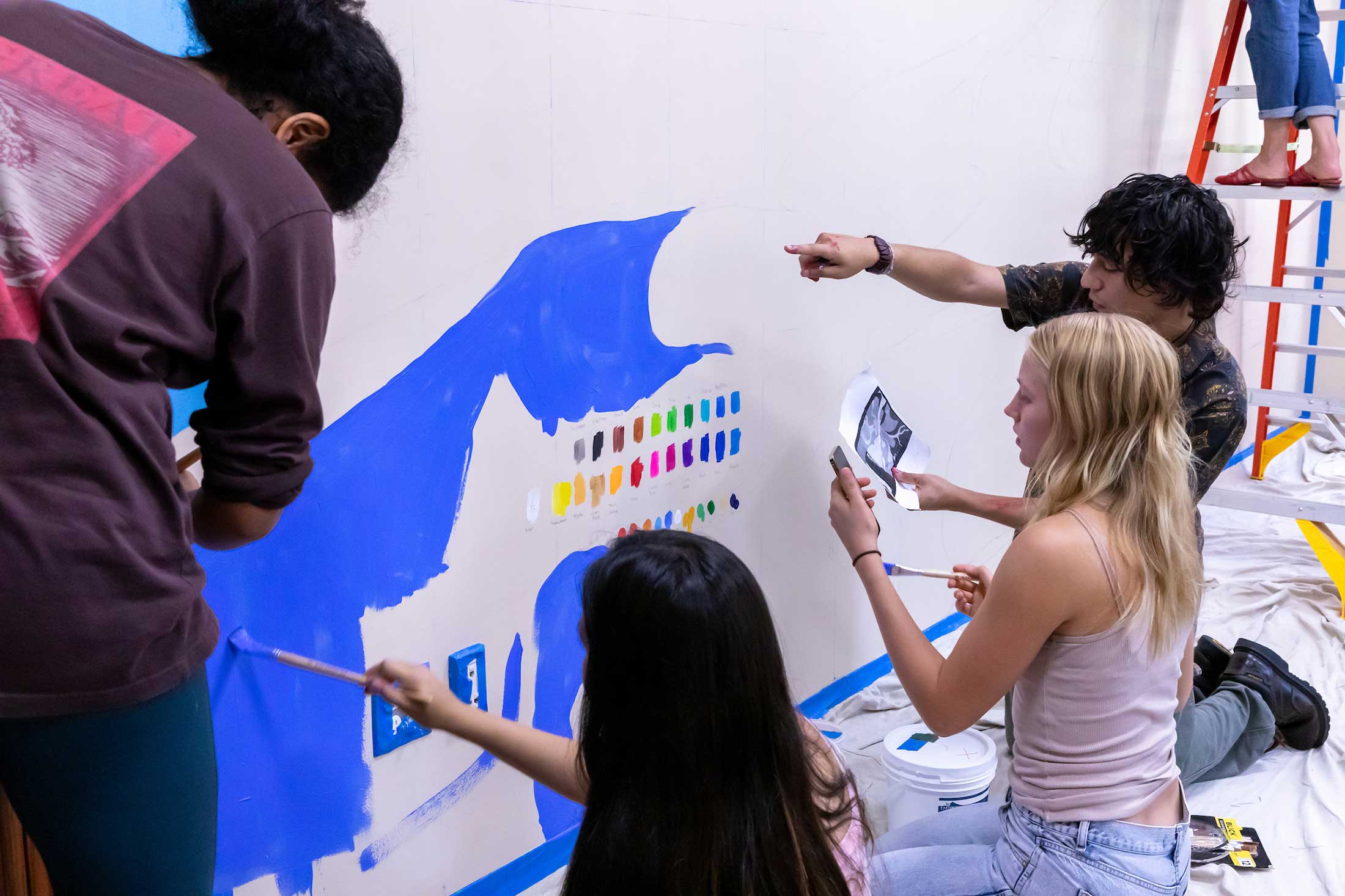 Four art students paint sections of the mural on a wall.