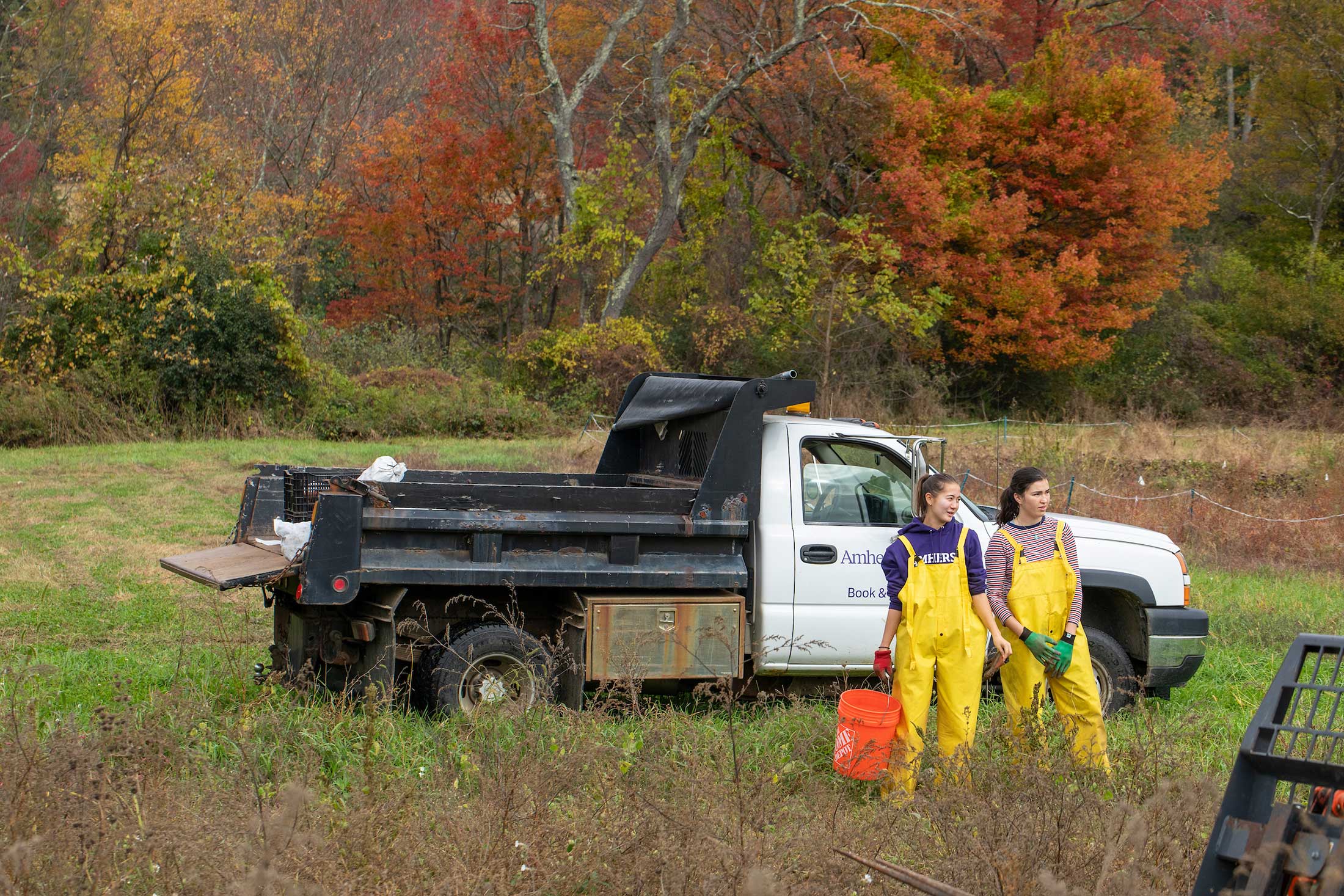 Two students stand in a field on the farm in front of a pickup truck.