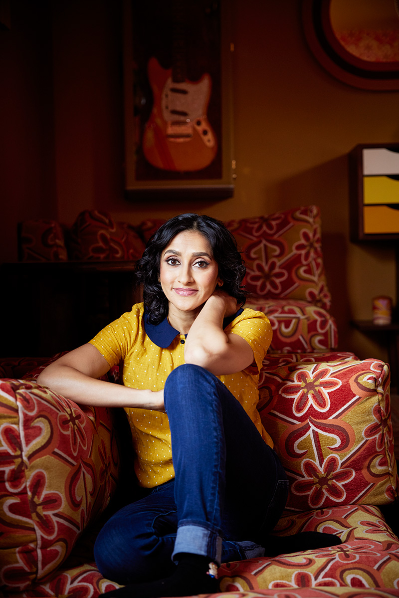 A woman in a yellow shirt and jeans sitting comfortably on a couch