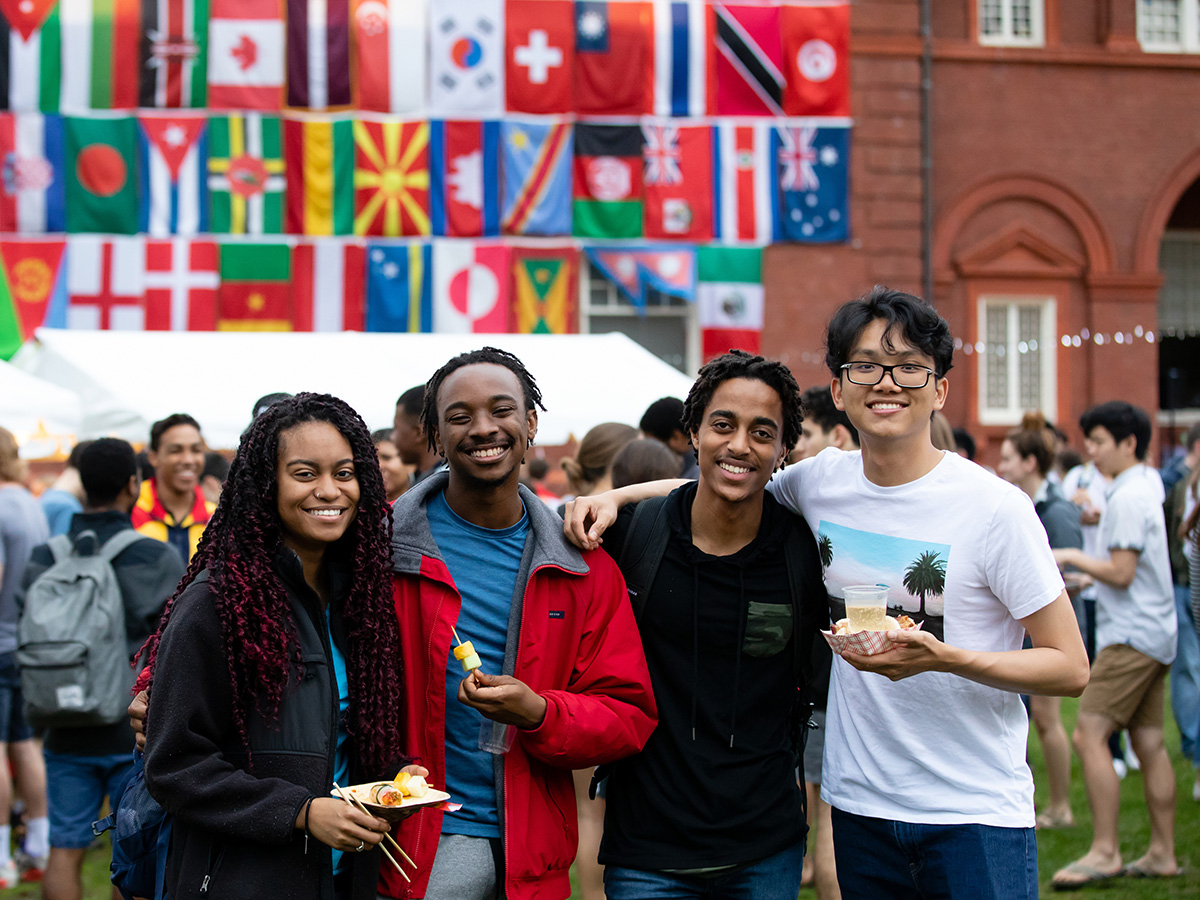 A group of four people holding food in front of a wall of flags
