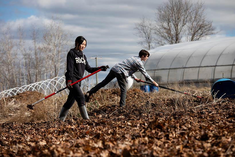 A student and a farm staff member raking in a garden