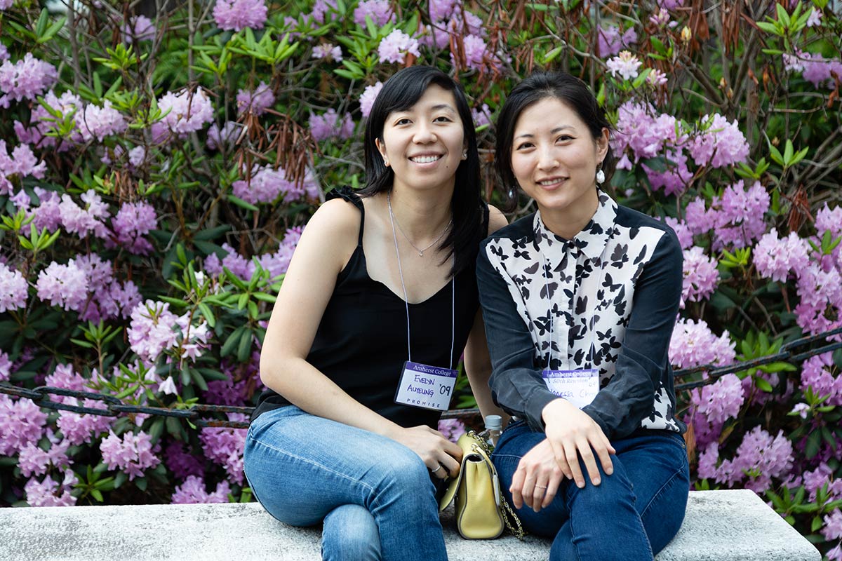 Two alumni sitting a bench side by side with pink flower blossoming behind them