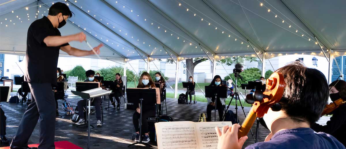 symphony orchestra students rehearse outside under a tent