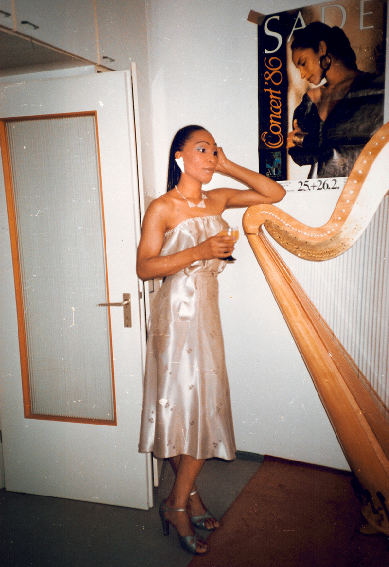 A woman in a dress leaning against a harp