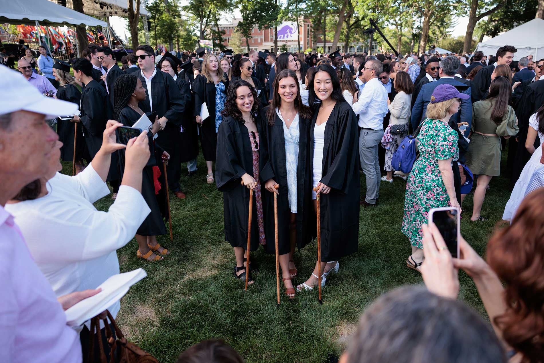 Three graduates pose for a photo in the middle of a crowd.