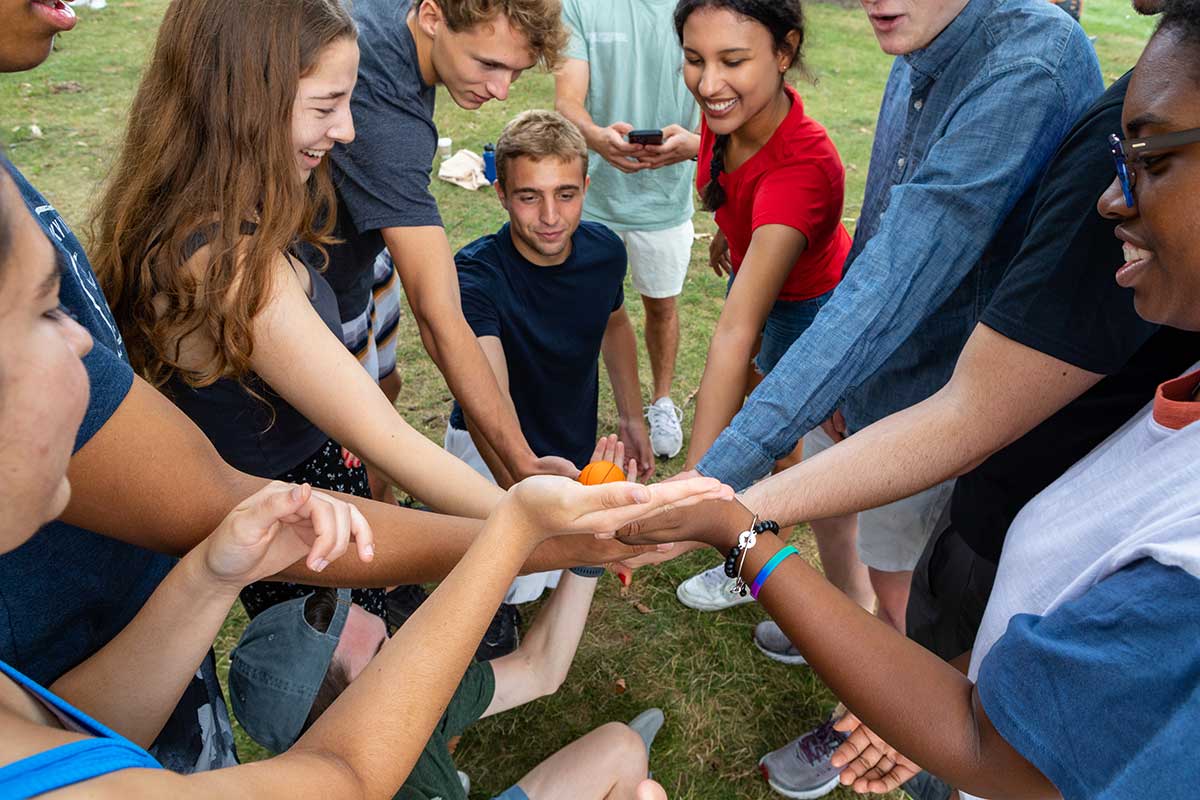 A group of students gather in a circle, placing their hands together in a stack.