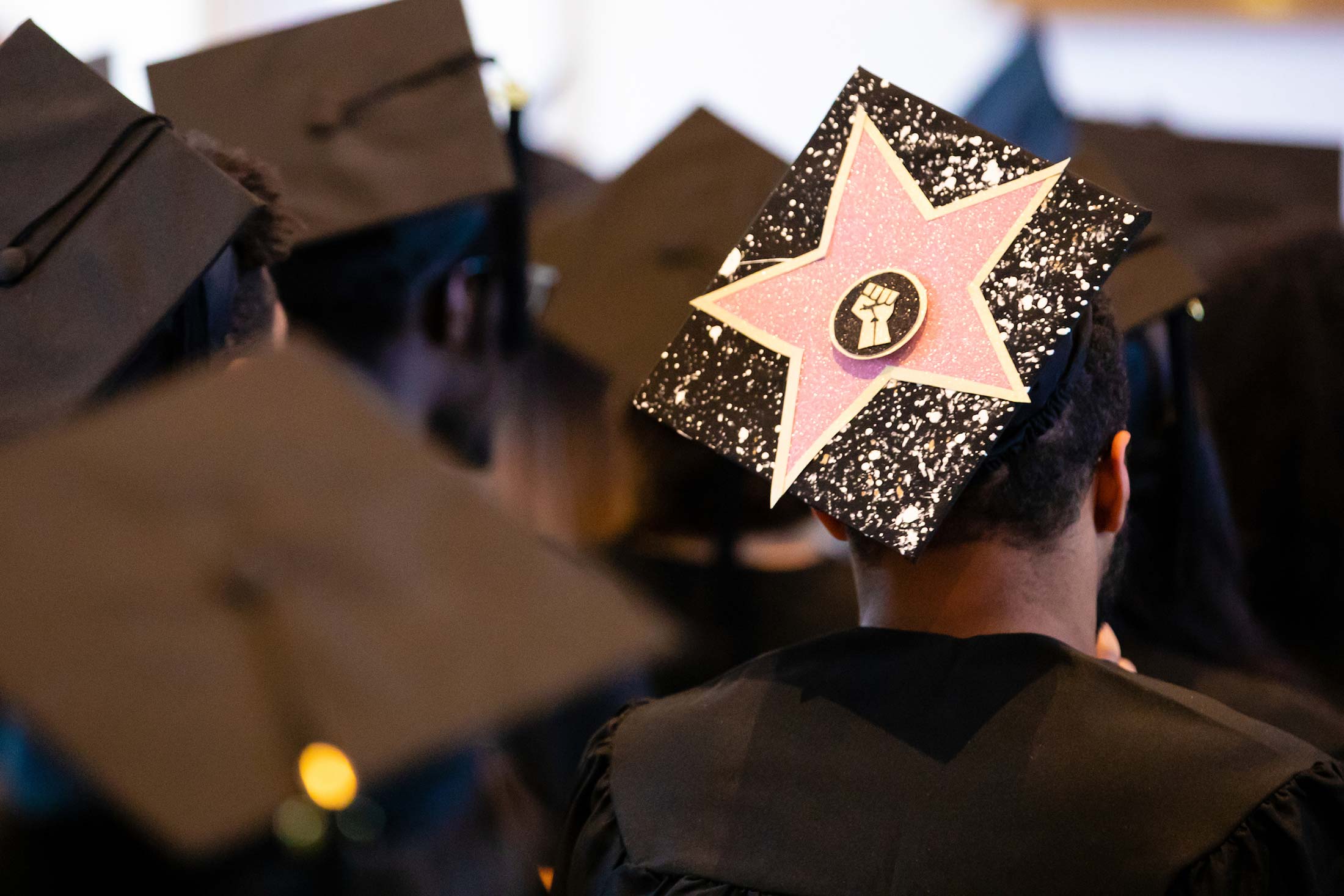 A close-up of a graduation cap decorated with a large pink star and a silhouette of a fisted hand