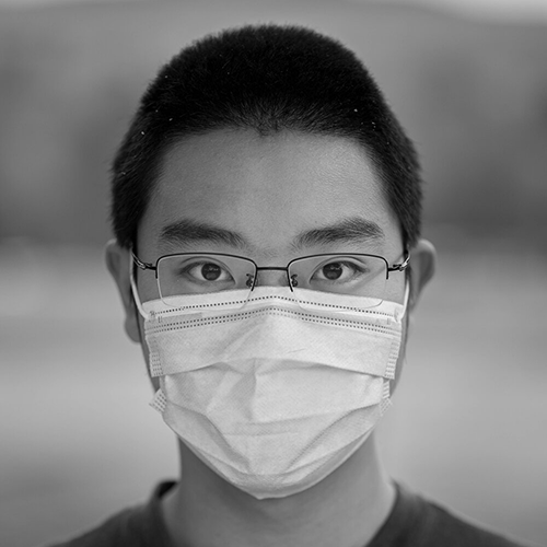 A black and white photot of an Asian man in glasses wearing a mask