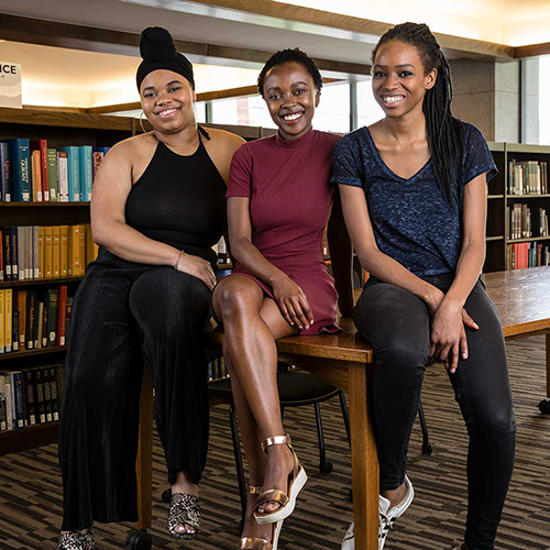 Three young woman sitting on a table in the Frost Library