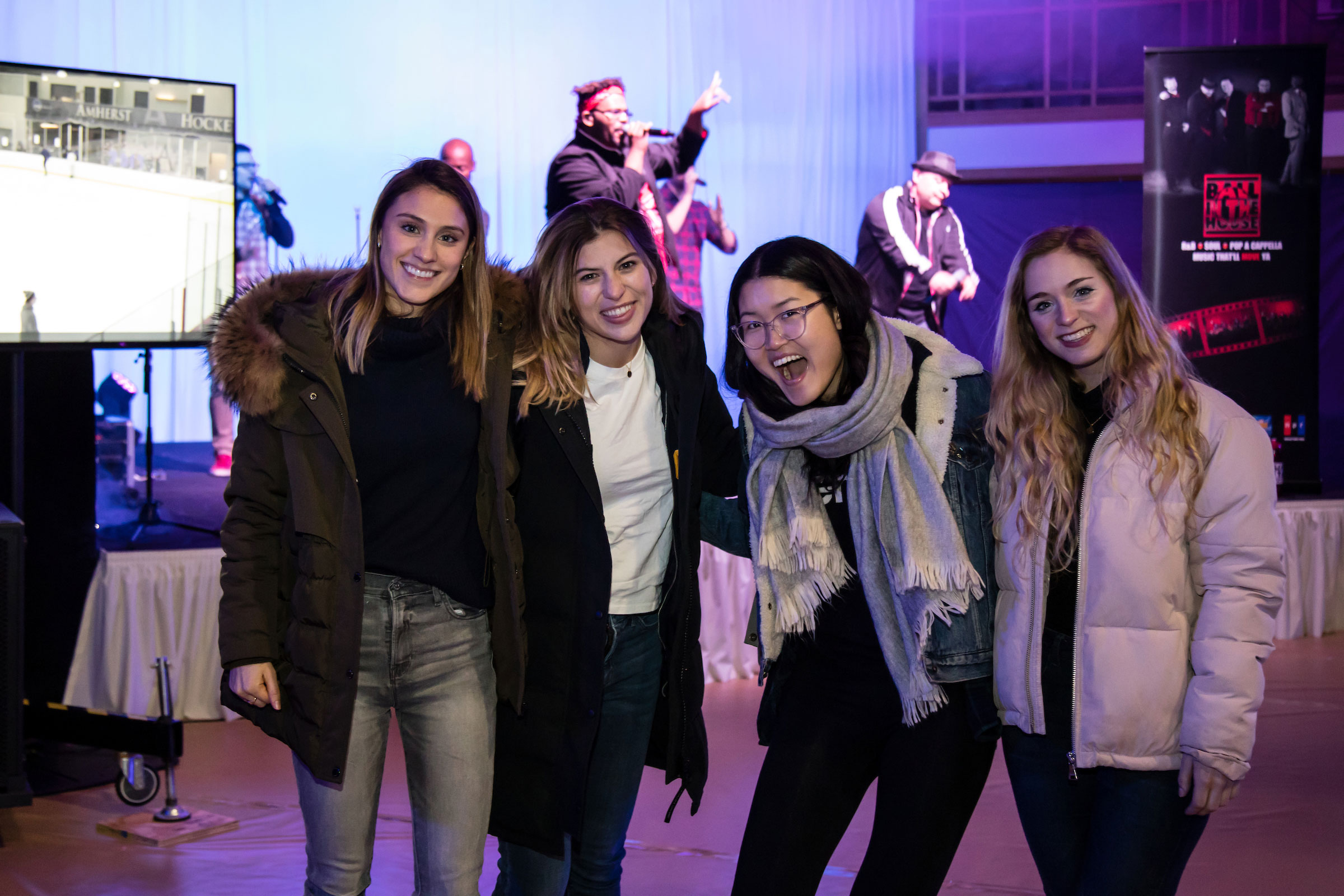 Four smiling women pose in front of the band at Winter Fest