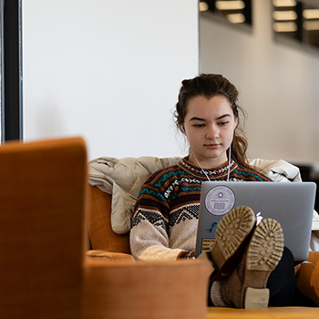 A young woman writing on a computer in an academic lounge