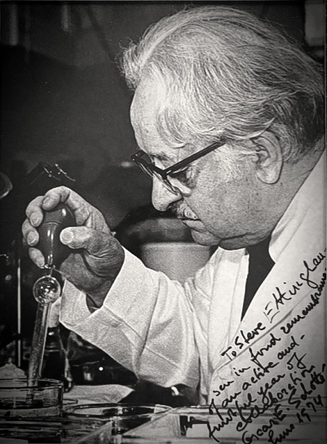 A black and white photo of an older man in galsses working with lab equipment