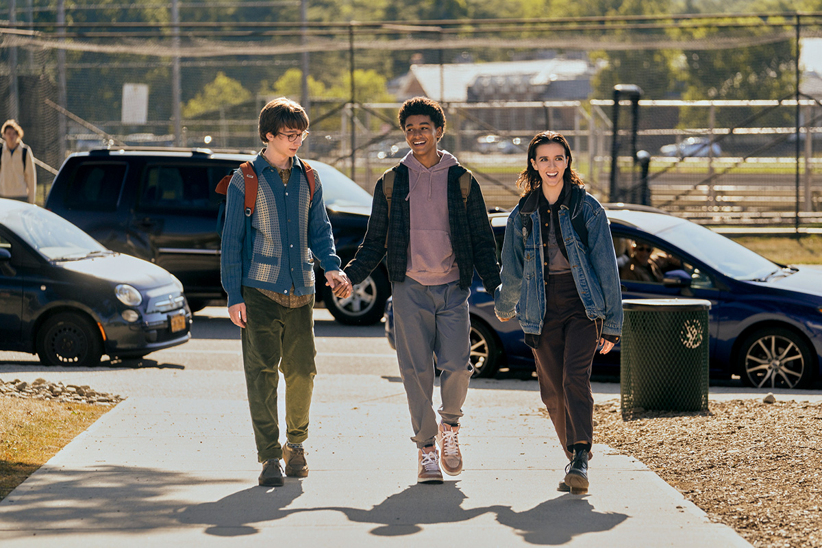 Three teenagers walking hand-in-hand down a sidewalk