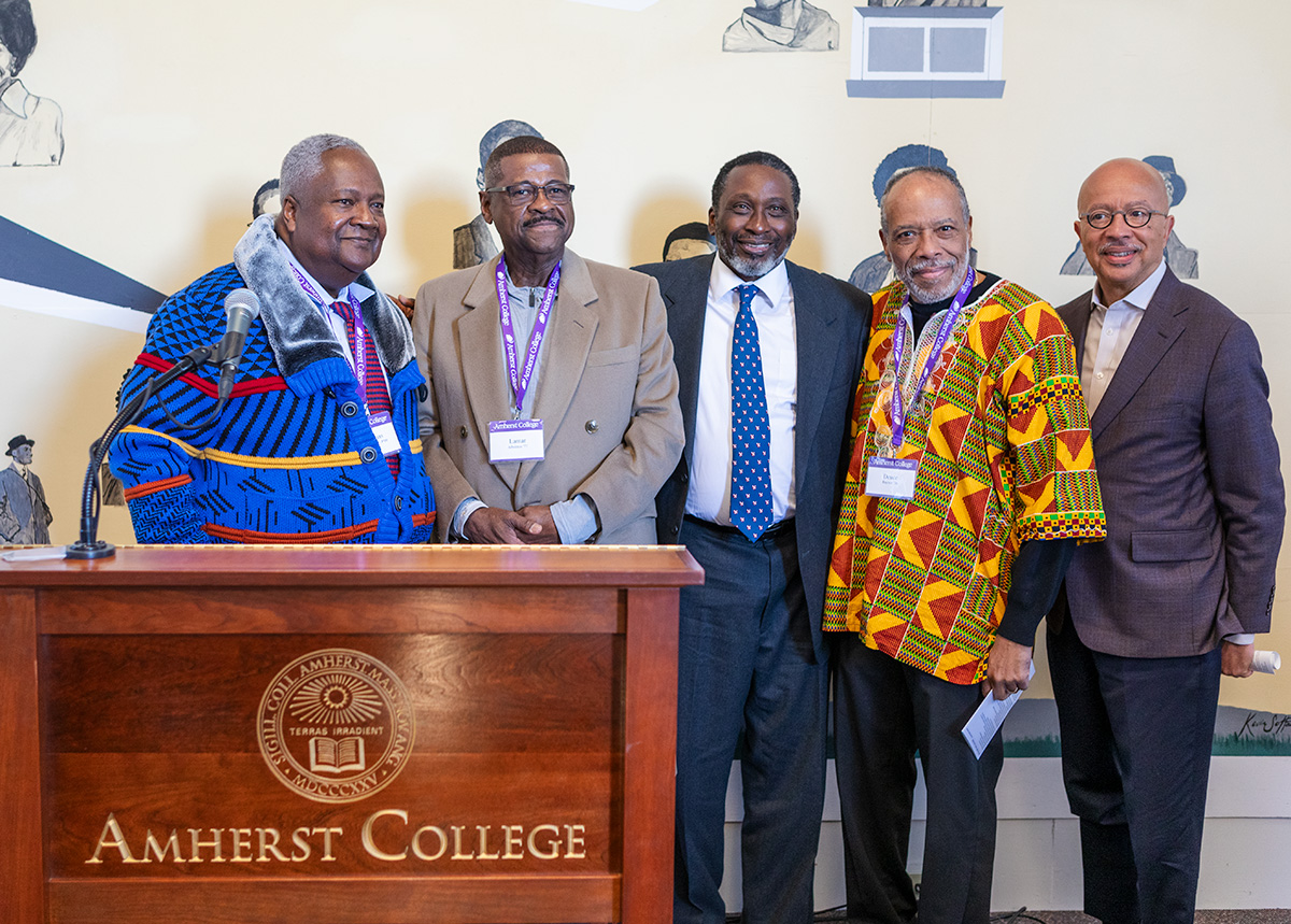 A group of Back men standing on a stage in front of an Amherst College podium