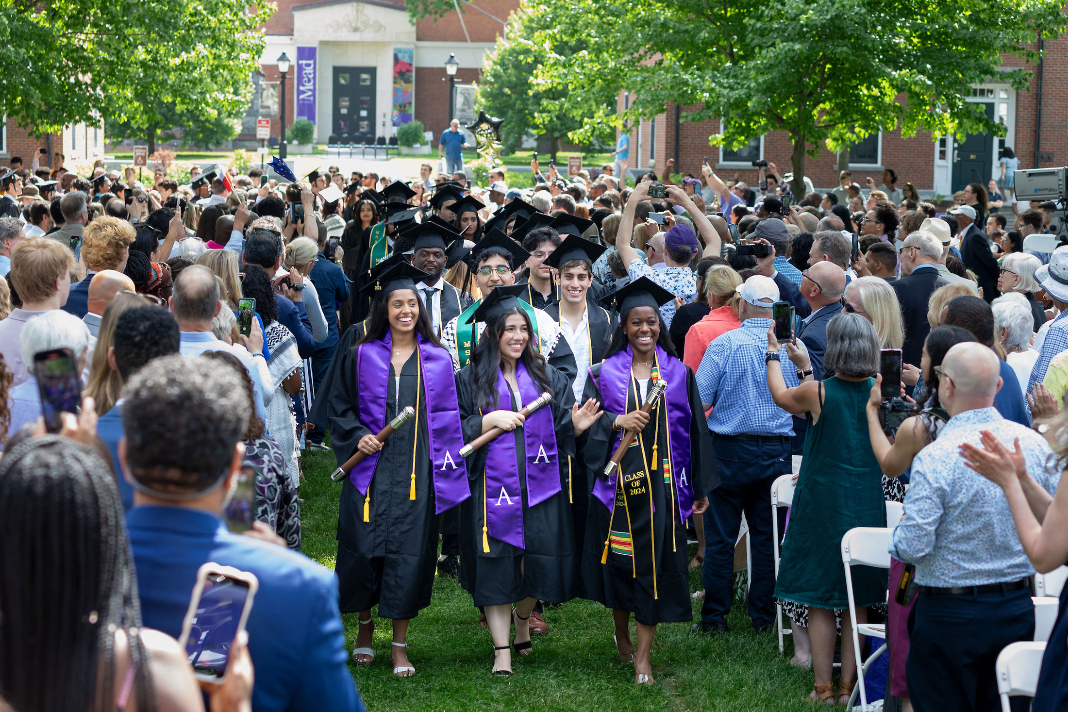 Three student marshals lead a procession of students through a crowd during commencement.