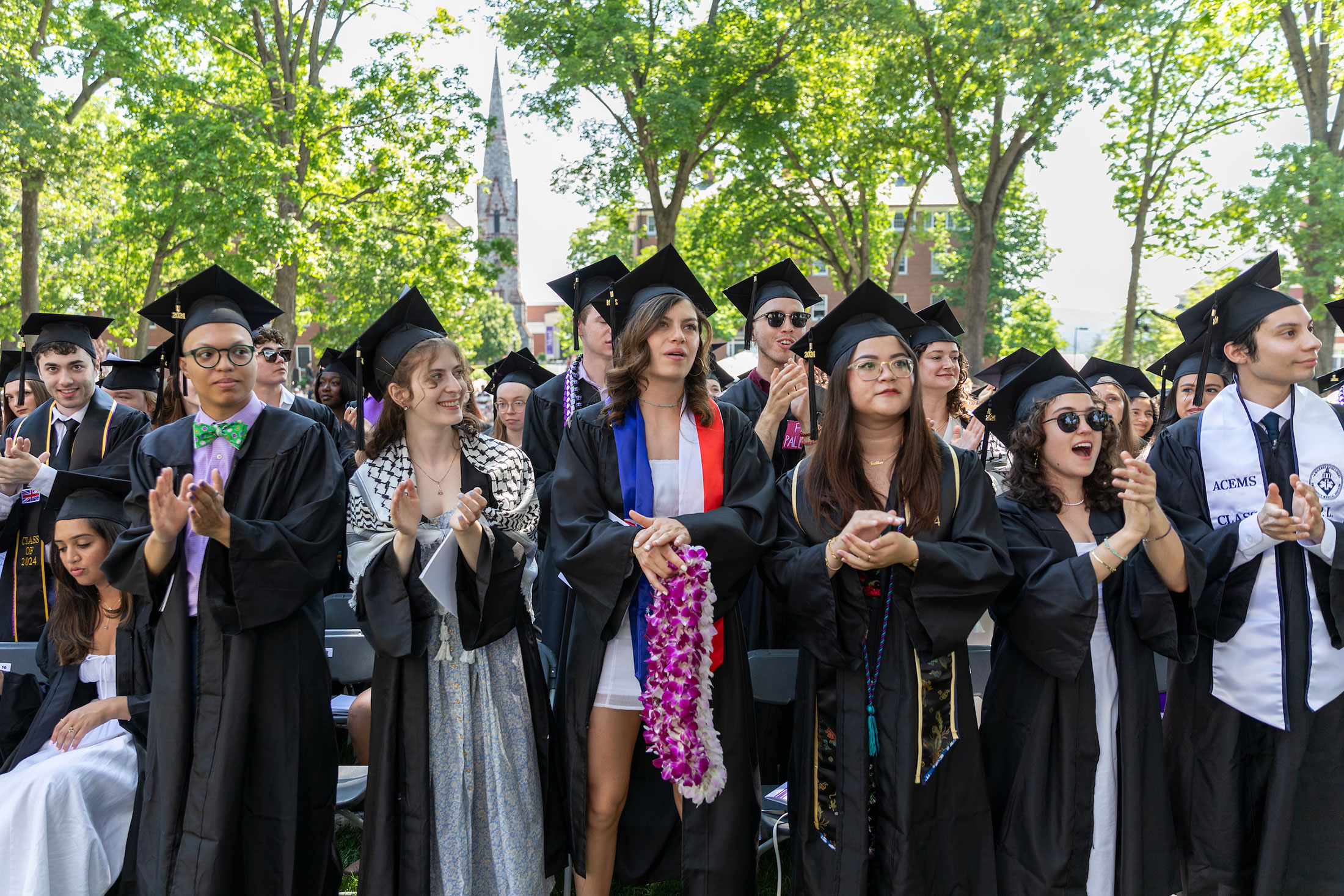 Students in graduation regalia stand and applaud during the ceremony.