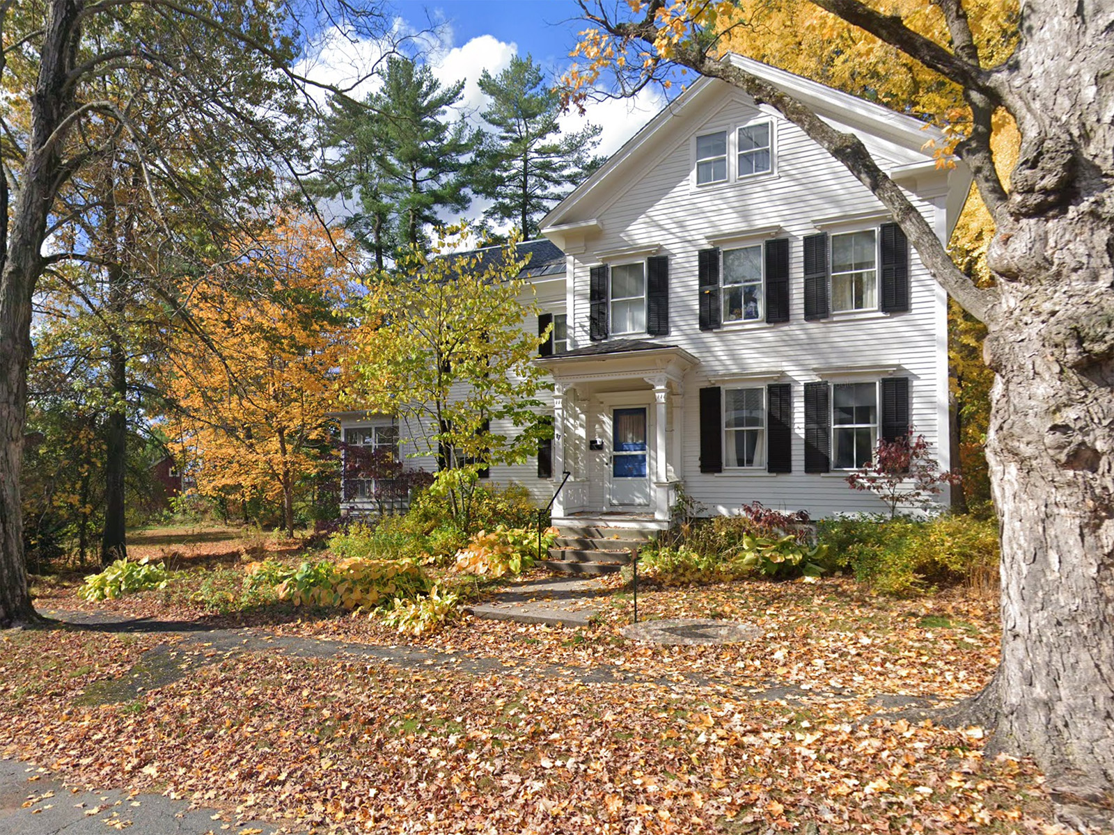 A two story white house surrounded by fall foliage