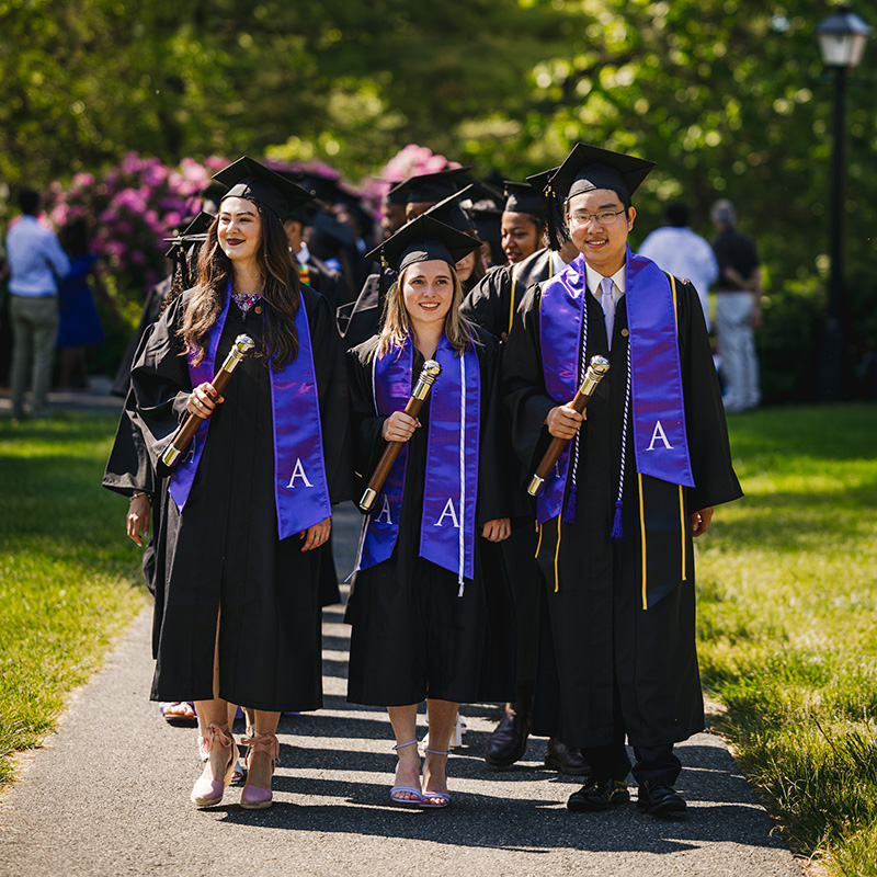 Three people in Commencement regalia carrying maces
