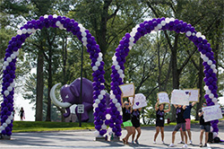 A group of students with welcome signs below purple and white arches