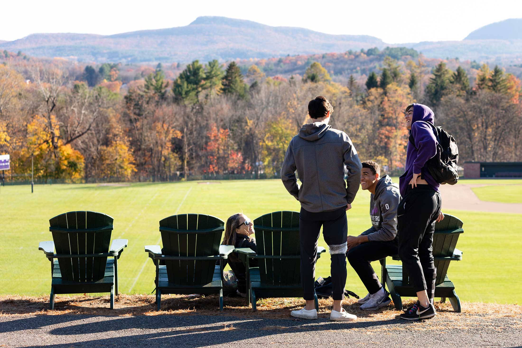 Four students gathered by the adirondack chairs overlooking the Mount Holyoke range