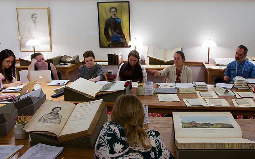 A group of people sitting around a conference table with large books open on the table