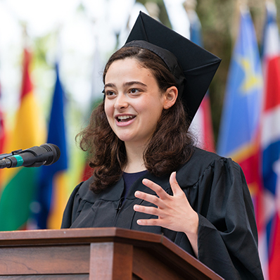 A young woman wearing a cap and gown speaking at commencement