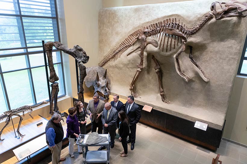 A group of people standing inside the Beneski Museum in front of a dinosaur