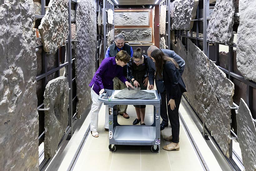 Five people leaning over a table examining the dinosaur trackway