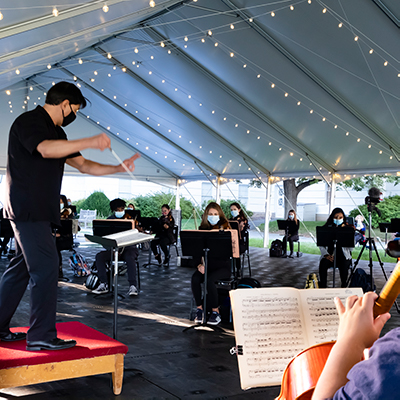 A conductor conducting an orchestra outside under a tent