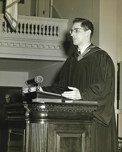 An old black and white photo of a young man speaking at a podium