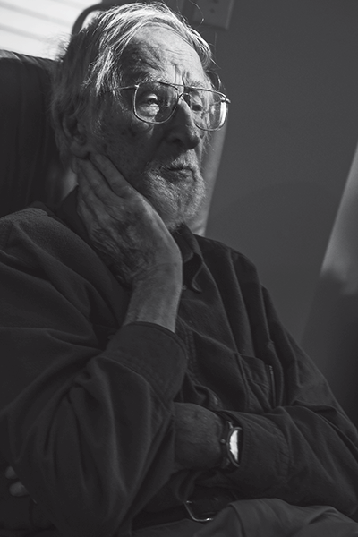 A black and white photo of an older man with his hand to his face staring into the distance