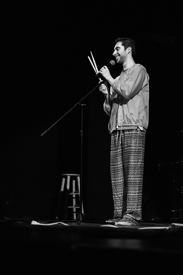A black and white photo of a stand up comic holding a pair of drumsticks