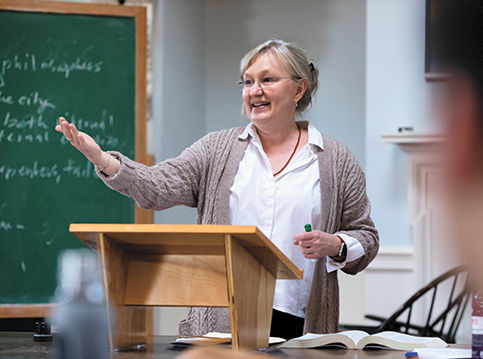 A woman speaking at a podium with a blackboard to the left
