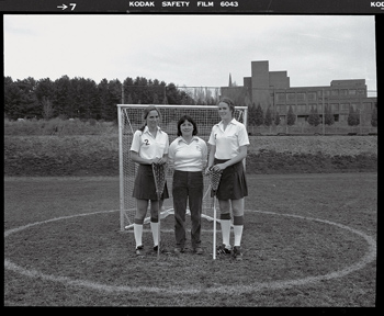 Katie Fretwell and two classmates in lacrosse uniforms standing in front of a goal post