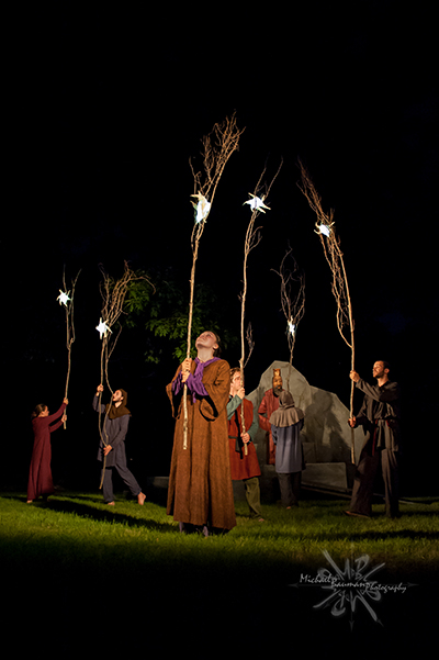 Actors hold branches with figures of moon and stars against the night sky