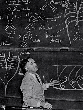 A black and white photo of a professor at a chaulkboard filled with equations