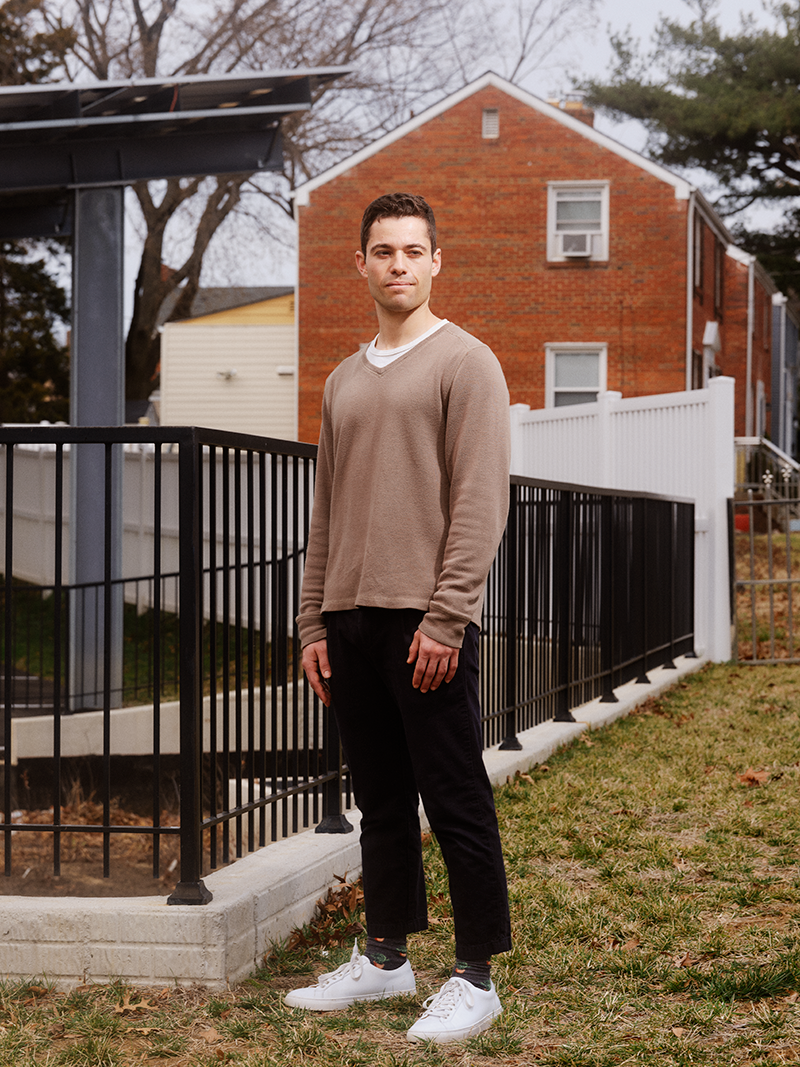 A man in brown sweater standing outside a house