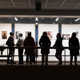 A group of people in silhouette look at an exhibit of black and white photographs. 