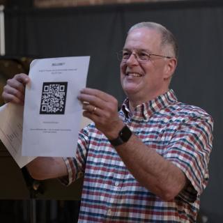 Director of Jazz Performance, Bruce P. Diehl laughing in plaid shirt, holds up a QR code