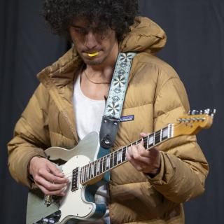 Young electric guitar player with tellow pick in his mouth
