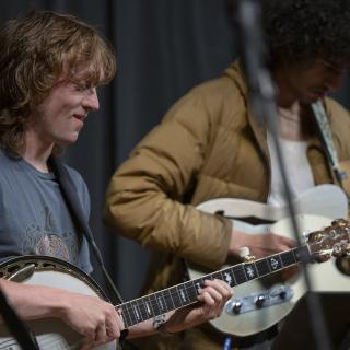 Two young players, playing: one smiling on banjo, the other in a down jacked on e-guitar