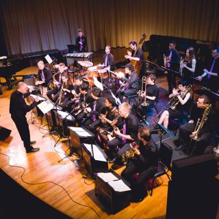 Bruce P. Diehl conducts the Amherst College Jazz Ensemble, dressed in black with prple ties, Buckley stage