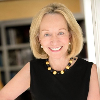 Closeup of Doris Kearns Goodwin smiling and wearing white pearl earrings, black-and-gold beaded necklace and black dress