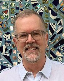 Man wearing glasses with a mosaic wall behind him