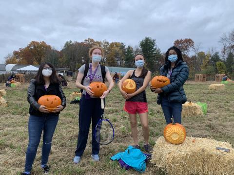 Four friends standing at the farm holding carved pumpkins